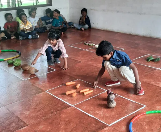 Interactive counting exercise with various vegetables on the classroom floor at Vidhya Peetham i-School in Salem.