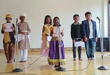 Eager third-grade students performing on stage with microphones during the Closet Drama Activity at Vidhya Peetham i-School, showcasing their talent in traditional costumes.