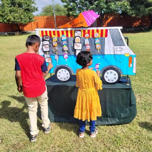 Grade 1 எழுத்துகளைக் கொண்டு சொல் உருவாக்குதல் 3_result Children at Vidhya Peetham i-School spelling out Tamil words with letter cards on an ice-cream vehicle chart, highlighting innovative learning methods.
