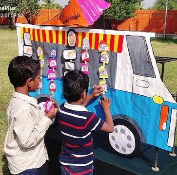 Two students from Vidhya Peetham i-School in Salem focusing on matching pictures with Tamil letters in an outdoor spelling activity session.