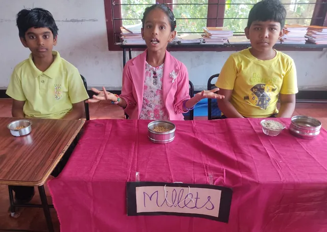 Eager Grade 4 students explaining about millets on a pink tablecloth, enhancing their knowledge about food crops at a Salem CBSE school.