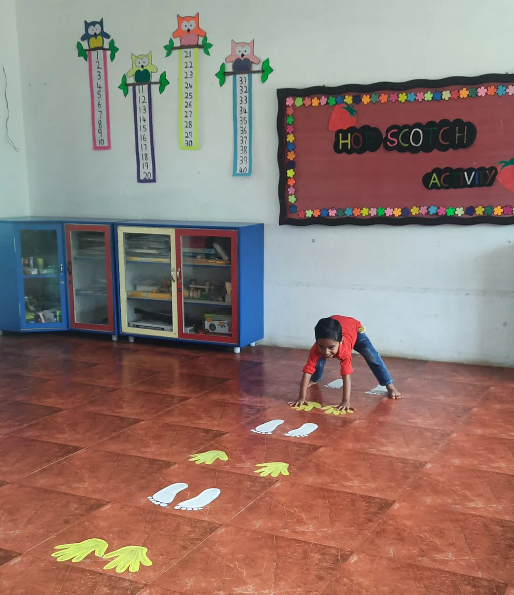 LKG student mastering balance and coordination in hopscotch kindergarten activity at Vidhya Peetham i-School, surrounded by colorful educational decor.