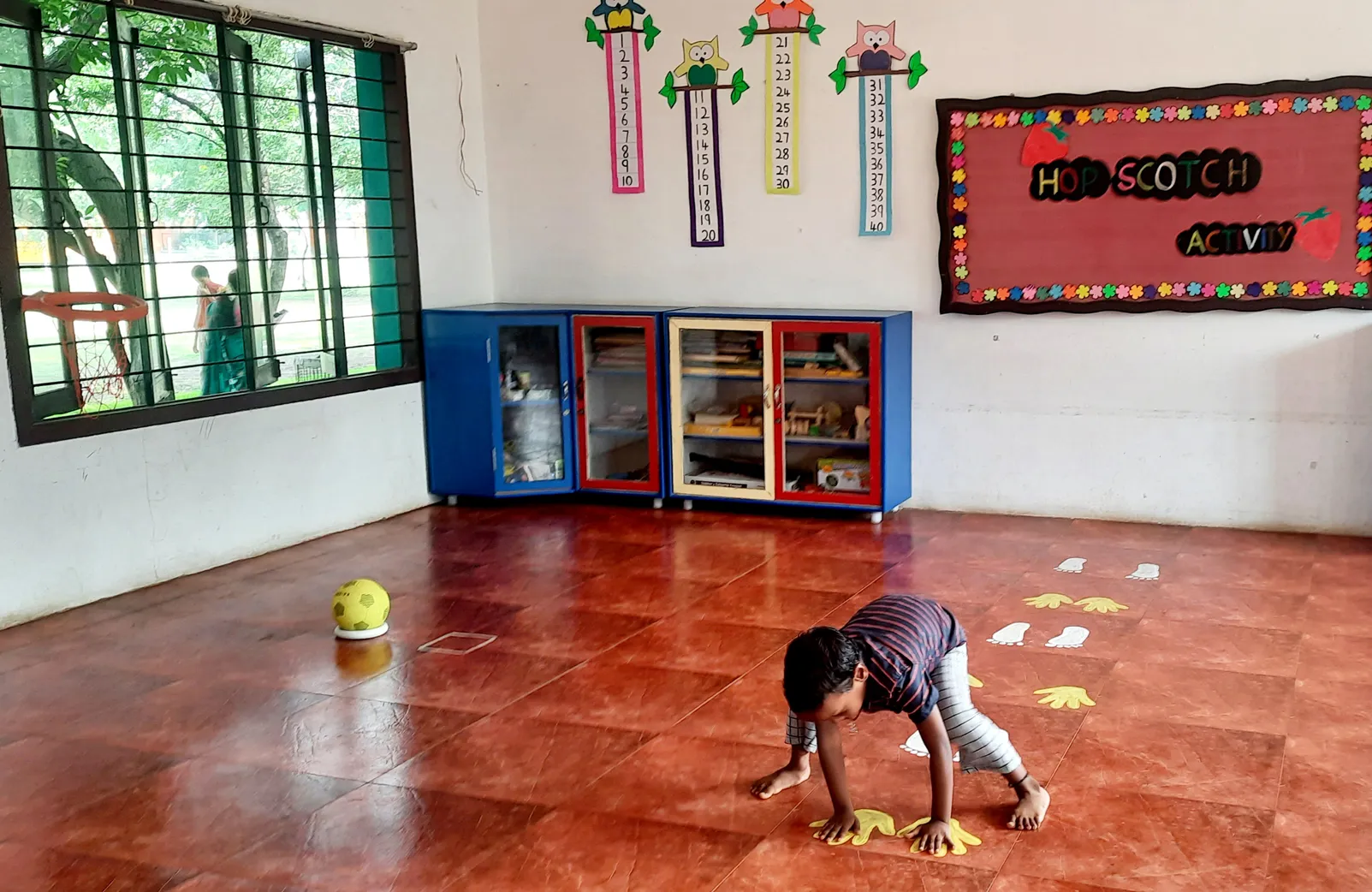 LKG Hopscotch activity 5_result Child crouching to match footprints during an interactive hopscotch game, promoting physical coordination at a leading Salem CBSE school.