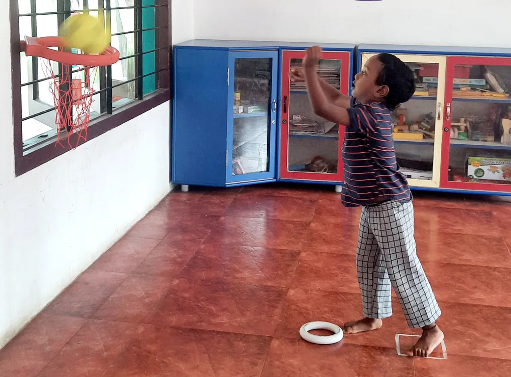LKG student at Vidhya Peetham i-School joyfully throwing a ball into a hoop, practicing hand-eye coordination in an innovative learning environment.