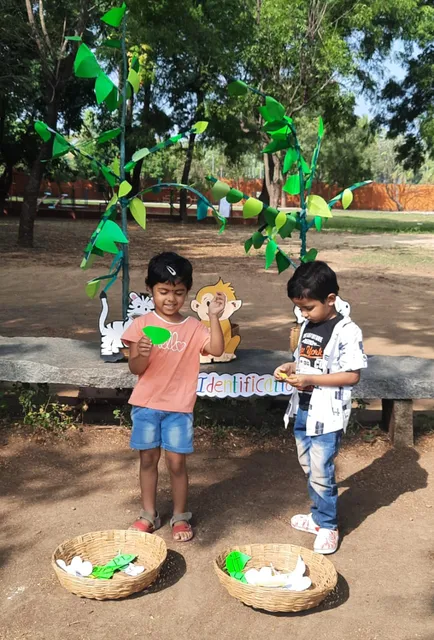 Vidhya Peetham i-School LKG class students collaborating in Spelling Fun activity, reading phonetic units and feeding animal charts in a playful outdoor setting.