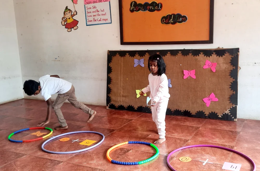 Young learners at one of the best schools in Salem performing math calculations using hula hoops and crafted paper butterflies during an interactive addition activity.