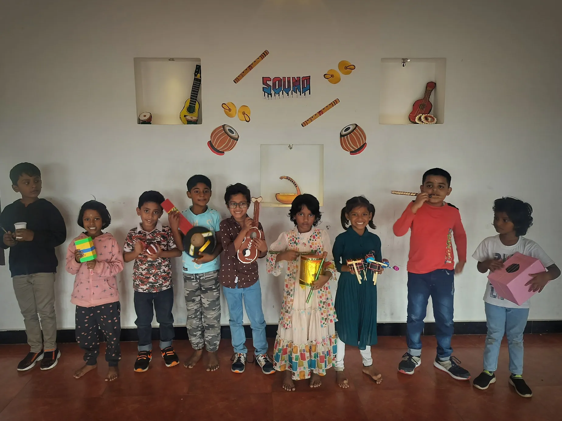 Proud young musicians from Vidhya Peetham i-School display their handmade instruments against a musical backdrop. ??
