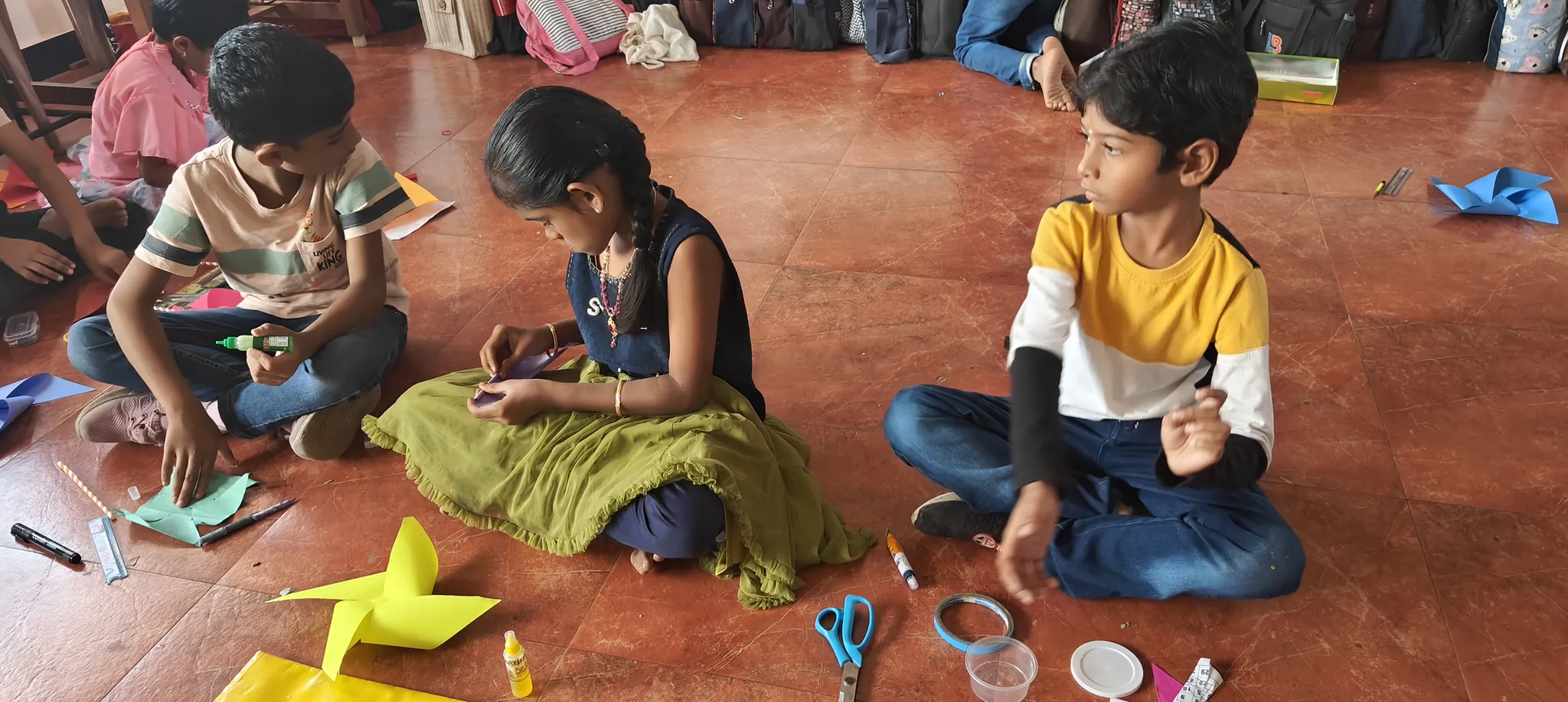 Engaged students sitting on the floor, intently assembling their eco-friendly pinwheels in a classroom.