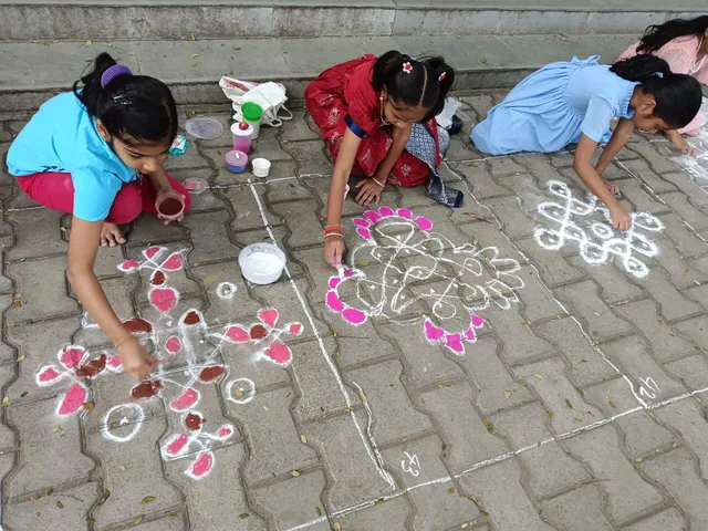 Group of young girls intently drawing traditional sikku rangoli kolam patterns on the school pavement, honing their artistic skills.