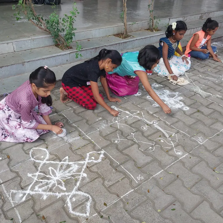 Schoolgirls in colorful attire skillfully creating sikku kolam with white powder, reflecting Vidhya Peetham i-School's commitment to cultural education.