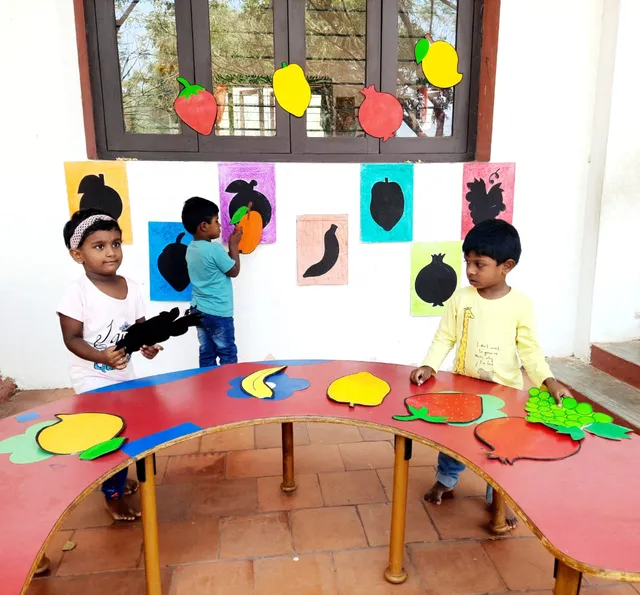 Young learners matching fruit flashcards to stencils on the wall, learning about different fruits at a Salem CBSE school.