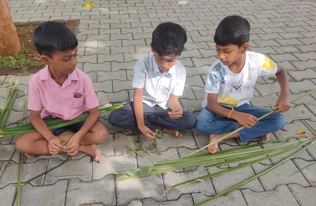 Three boys carefully weaving coconut leaves to create crafts at Vidhya Peetham i-School.