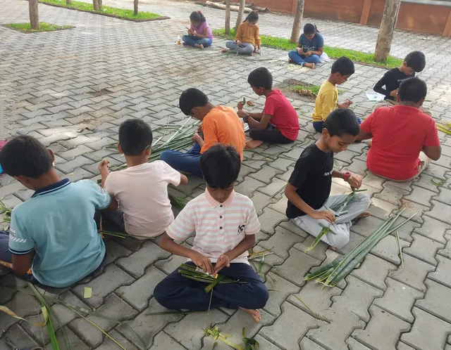 Group of students proudly displaying their coconut leaf crafts under a tree at a Salem school.