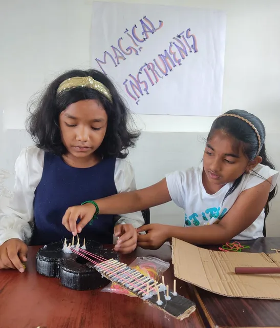 Two girls crafting a string instrument labeled "Magical Instruments" during the Grade 5 activity. 4.