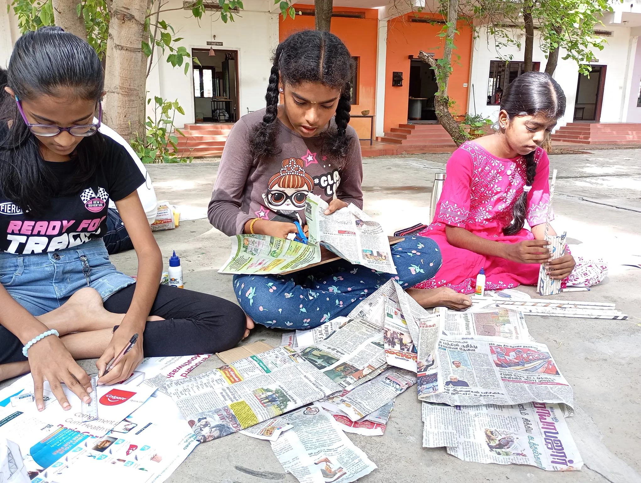 Three girls crafting with newspapers in an outdoor setting at a Salem school.