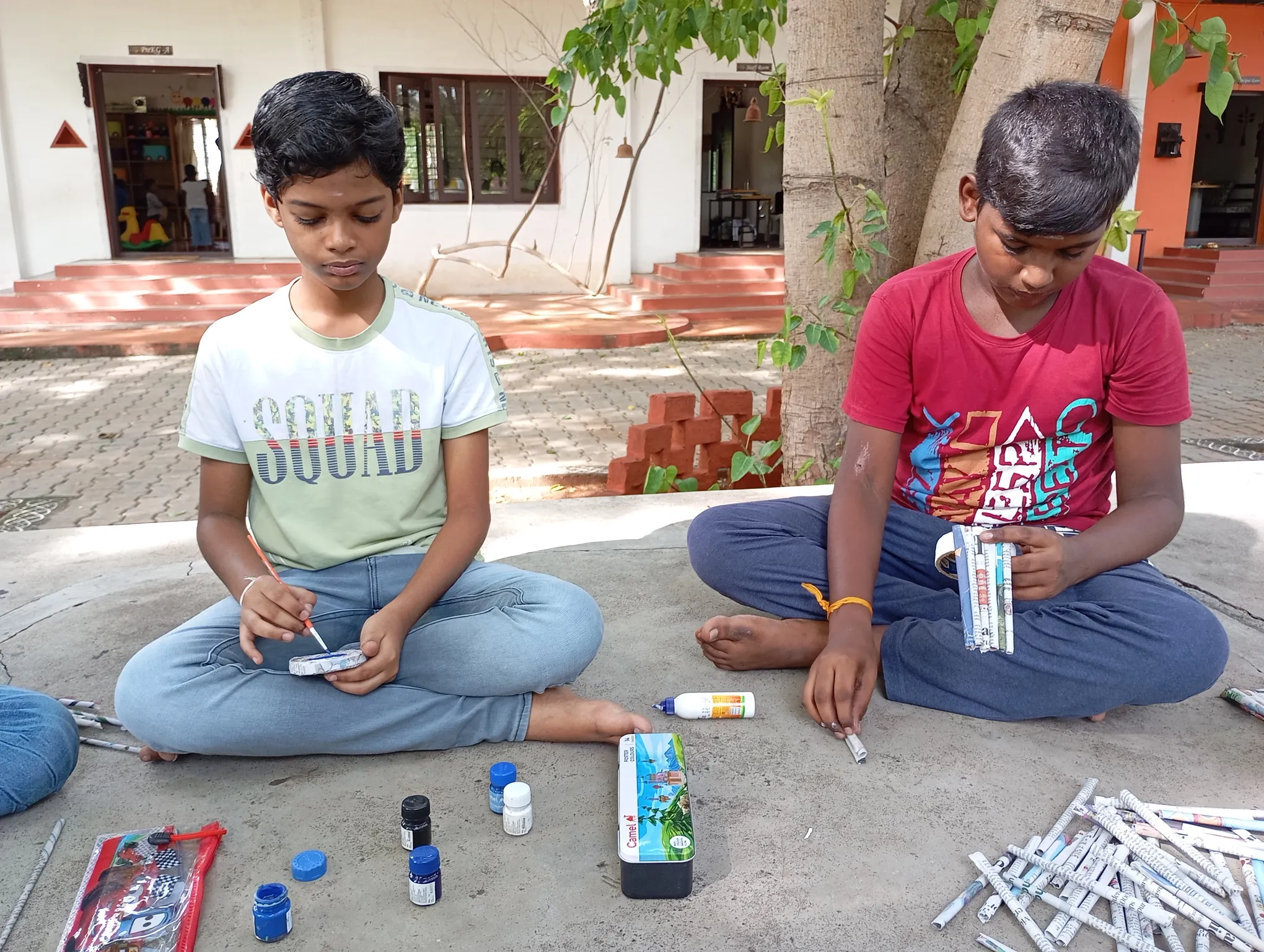 Two boys cutting and pasting rolled newspapers for a craft project.