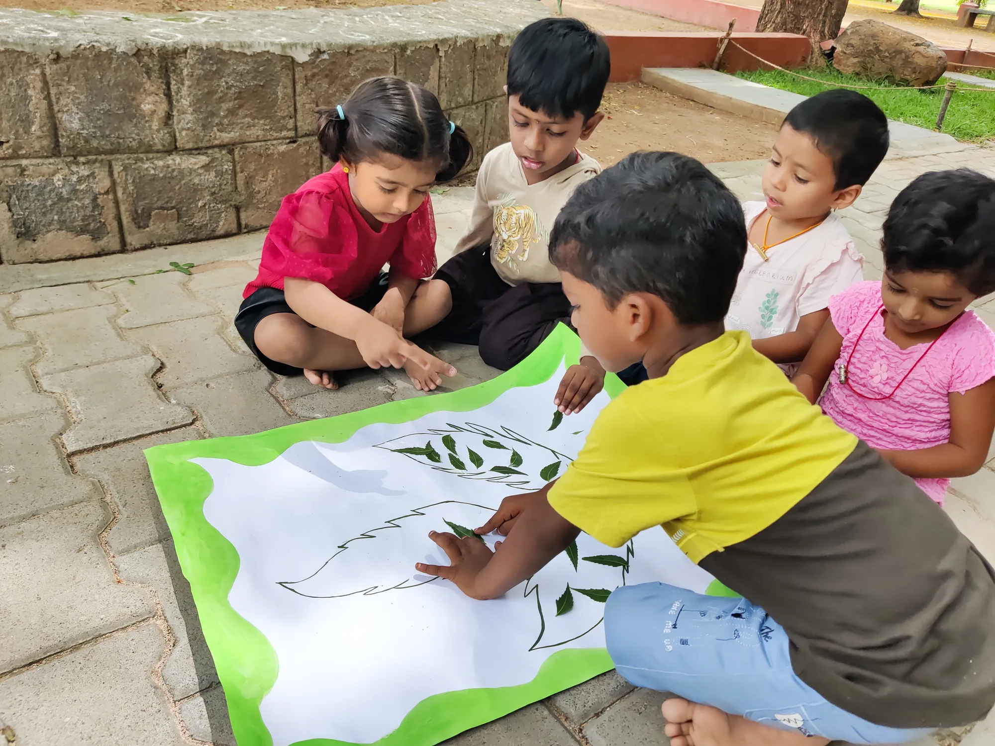 Group of LKG students proudly displaying their neem leaf artwork.