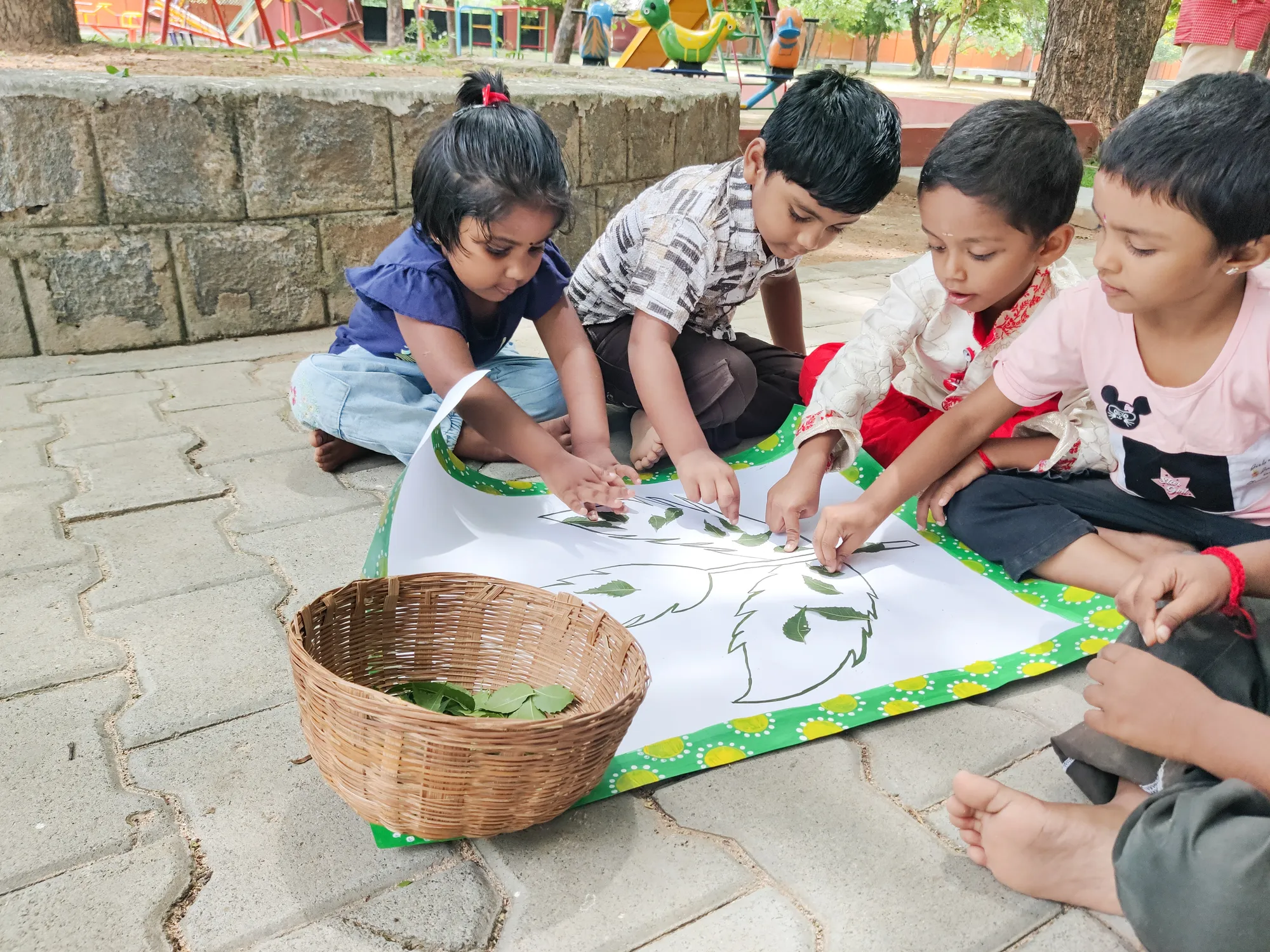 LKG students pasting neem leaves on a stenciled chart.