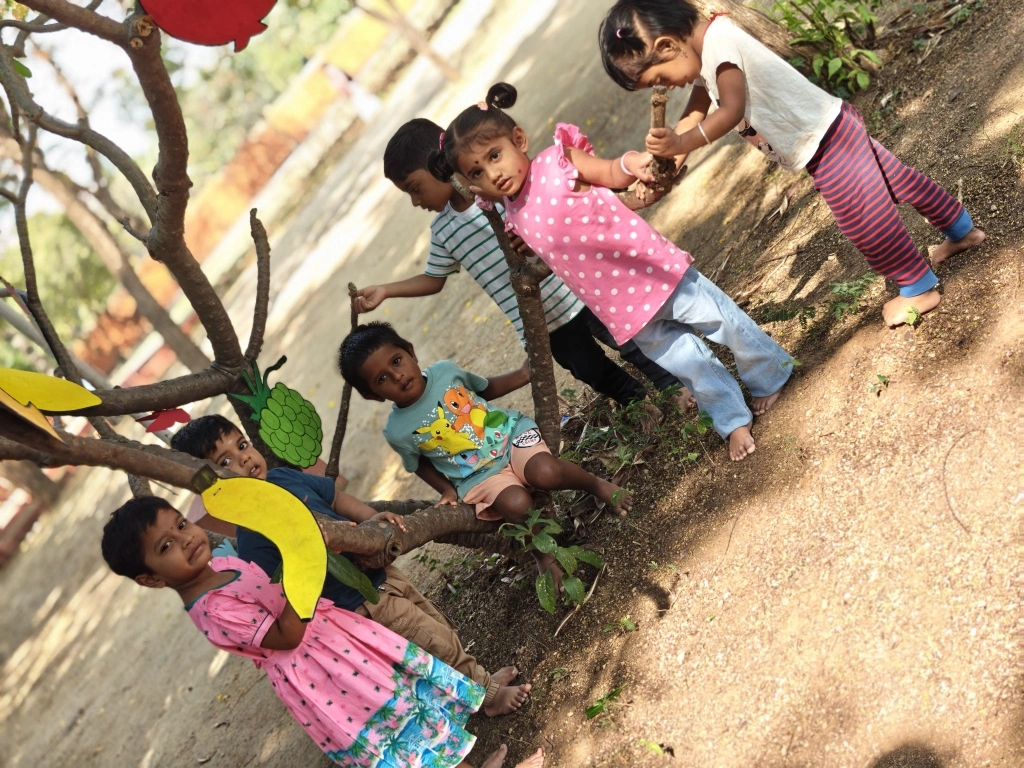 Children exploring fruit cards on decorated tree branches during the educational activity
