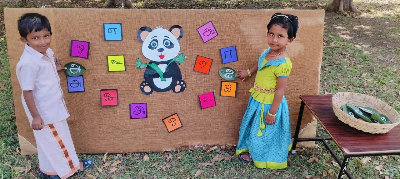 Students actively participating in Tamil letter identification activity with panda-themed board