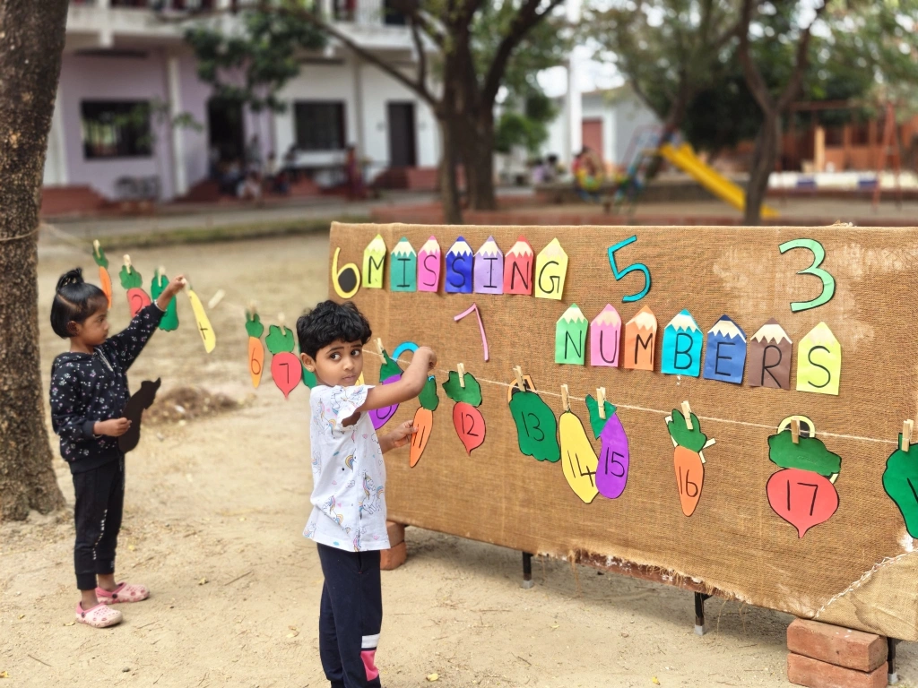 Student at Vidhya Peetham i-School engaging with colorful number cards on a brown display board during missing number activity