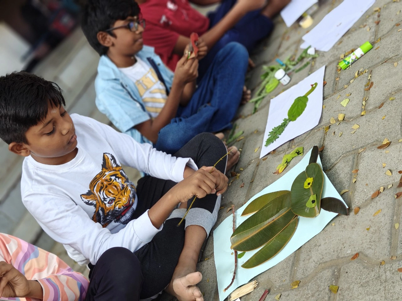 Student in white t-shirt carefully crafting a leaf art design, showing attention to detail