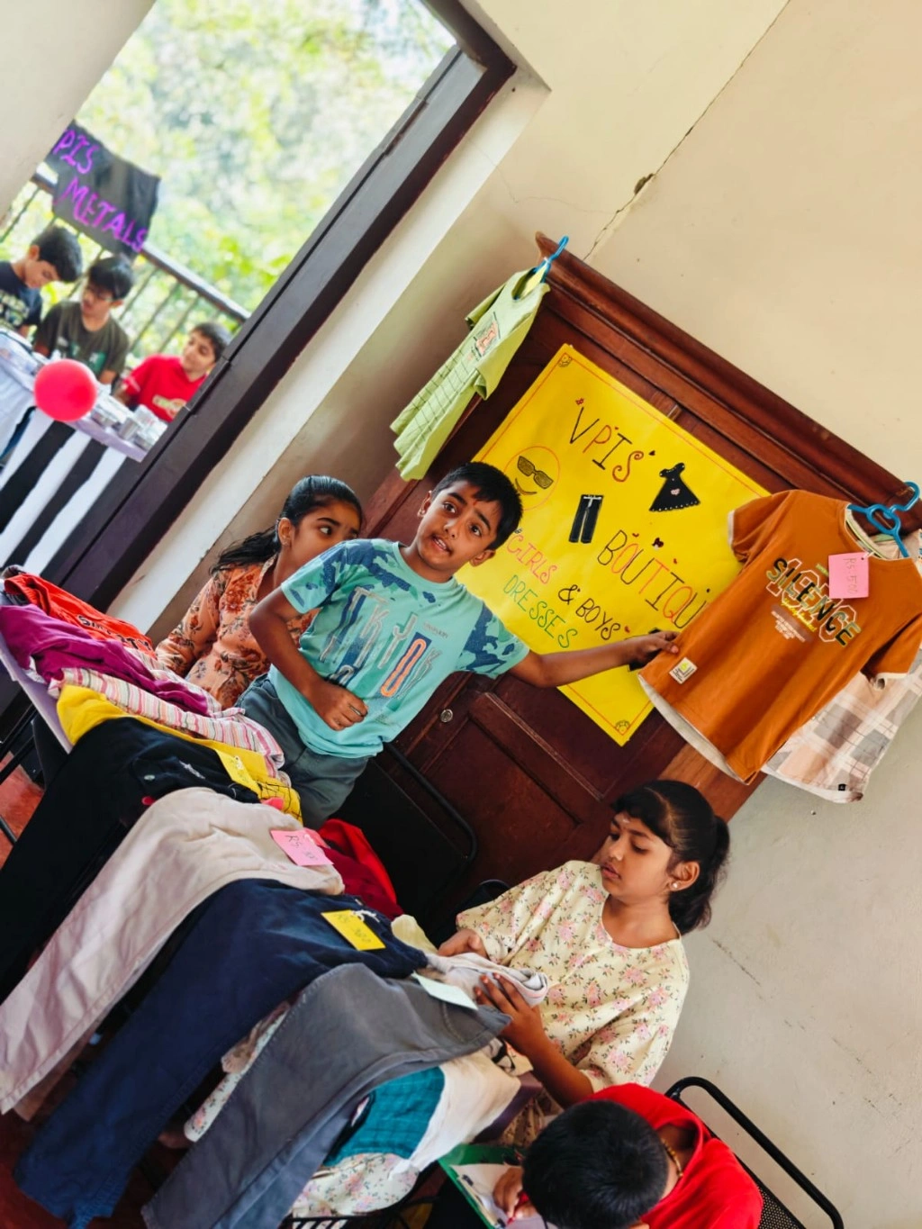 Students managing a boutique stall with colorful clothing displays and price tags at VPIS math activity fair