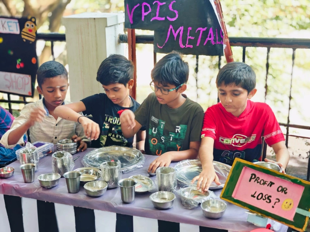 Students calculating profits using metal utensils and price tags at VPIS math fair